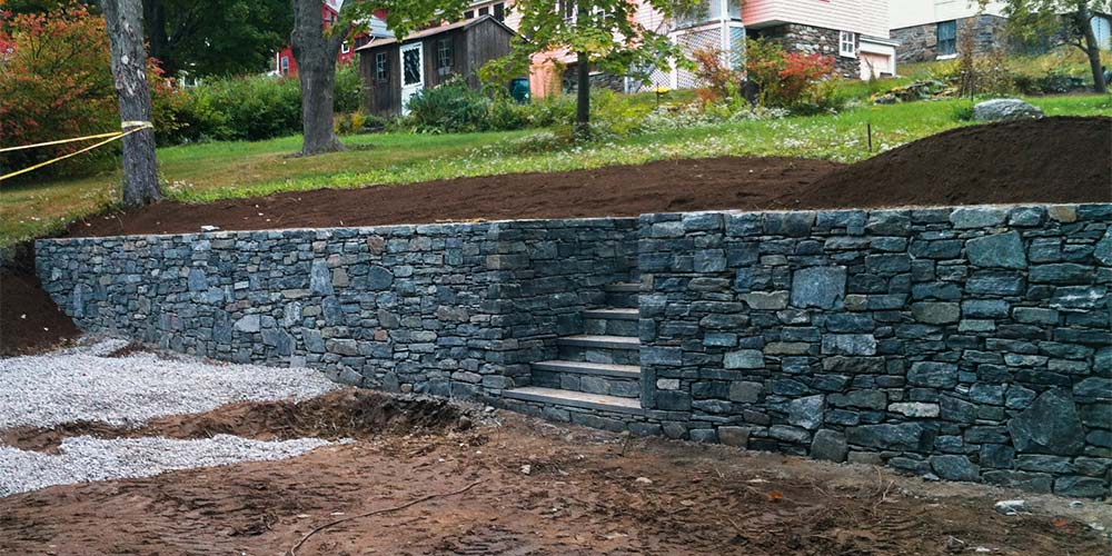 Grading with stone retaining wall with built-in steps leading up to a grassy yard beside a house